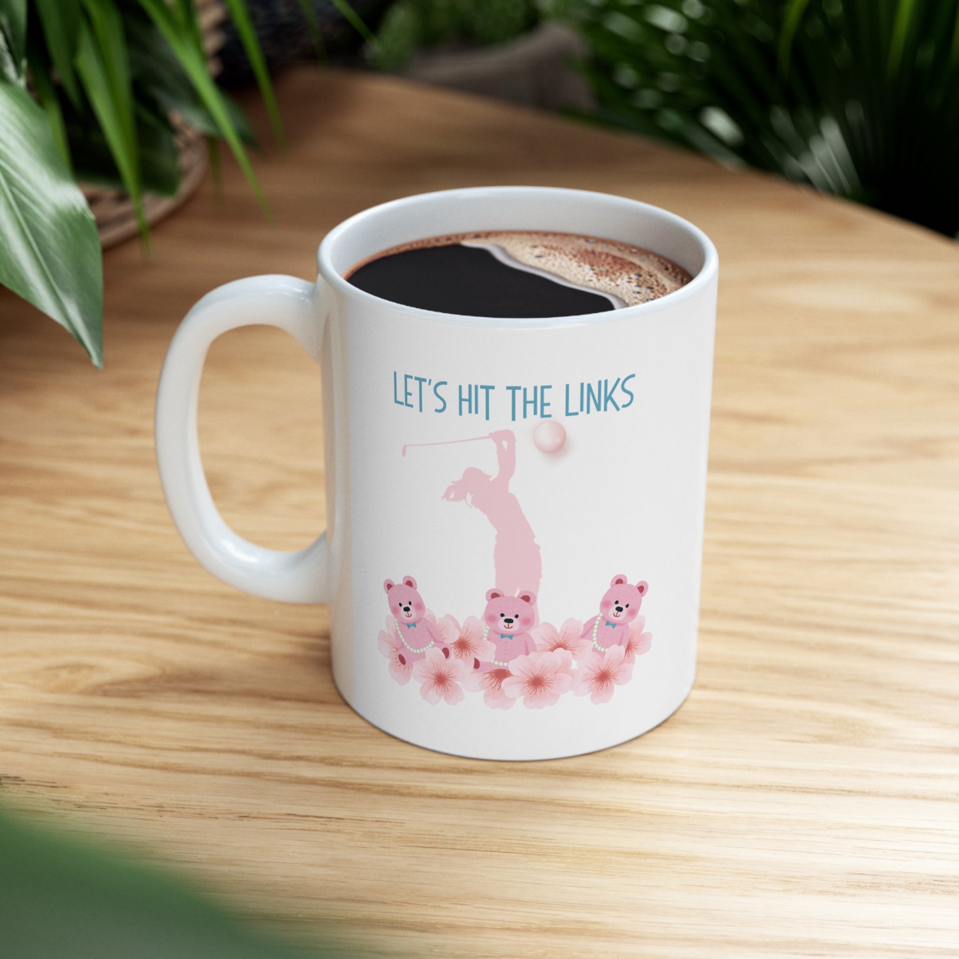 Tee off your day with this charming 11-ounce ceramic coffee mug. The playful design showcases adorable teddy bears surrounded by blooming light pink flowers. 